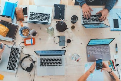 Content marketing is vital for small businesses. People sitting down near table with assorted laptop computers.